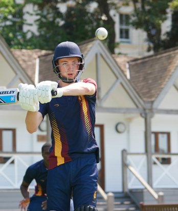 Pupil in cricket kit in front of the Sammy Woods Pavilion on the Home Ground holding their bat up and preparing to hit a cricket ball