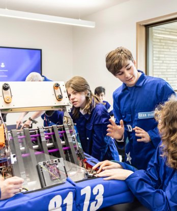 Pupils in blue boiler suits examining a piece of machinery in Robotics with Gear Zero