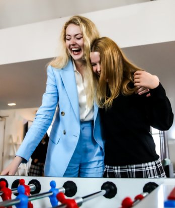 Boarding pupils in New House Common Room with their arms around each other and playing table football