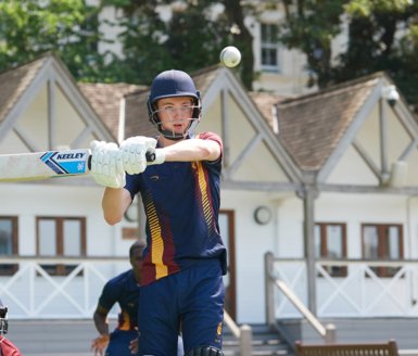  Pupil in cricket kit in front of the Sammy Woods Pavilion on the Home Ground holding their bat up and preparing to hit a cricket ball 