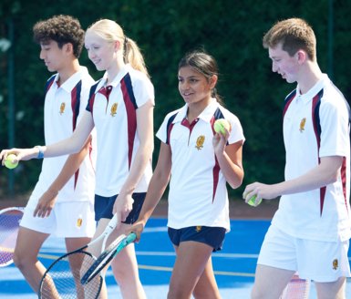  Pupils holding rackets and balls and walking down the Tennis Court 
