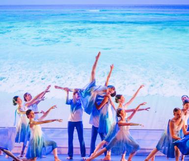  Pupils in flowy outfits performing a sea themed dance on stage 