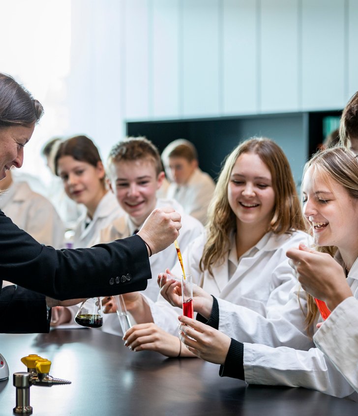  Pupil holding a test tube that the Biology teacher is adding a substance to as part of a Biology experiment 