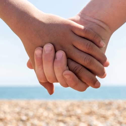  Pupils holding hands on the beach with a view of the stones and the sea 