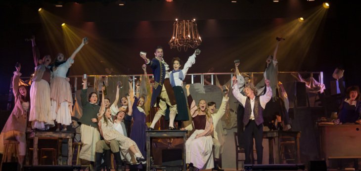  Pupils in the Les Misérables Cast standing on tables and chairs on stage in their performance 
