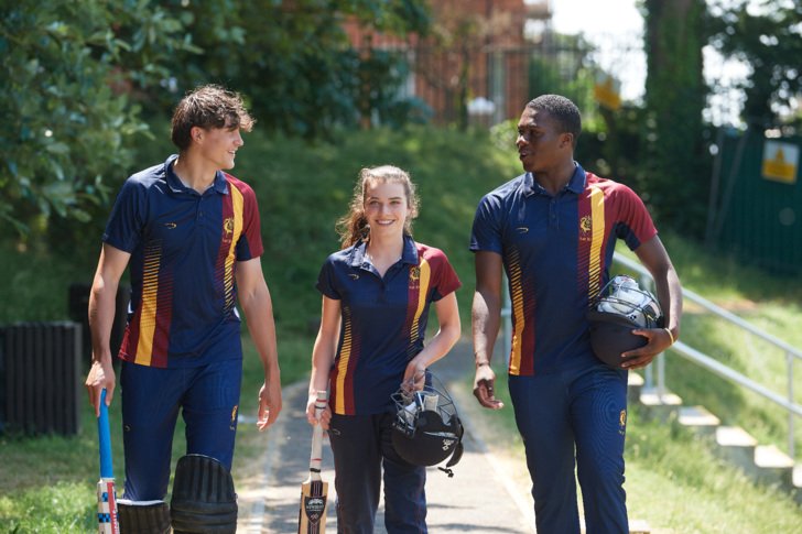  Cricketers in their kit holding cricket equipment walking along the Home Ground 