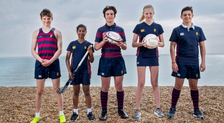  Pupils in games kit on the beach holding different sports equipment 