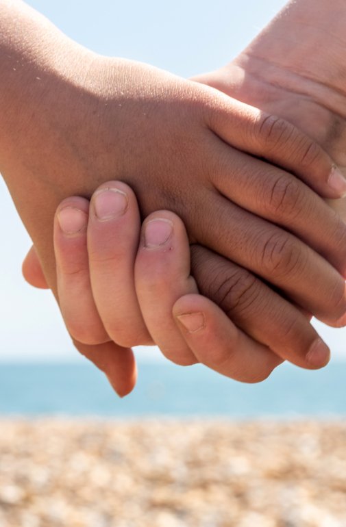  Pupils holding hands on the beach with a view of the stones and the sea 